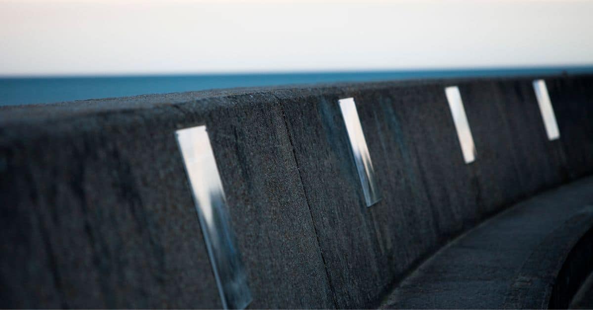 A detailed close-up of a massive reinforced concrete sea wall featuring vertical metal inserts for structural integrity and monitoring.